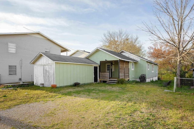 rear view of property with fence, a storage shed, an outdoor structure, and a yard
