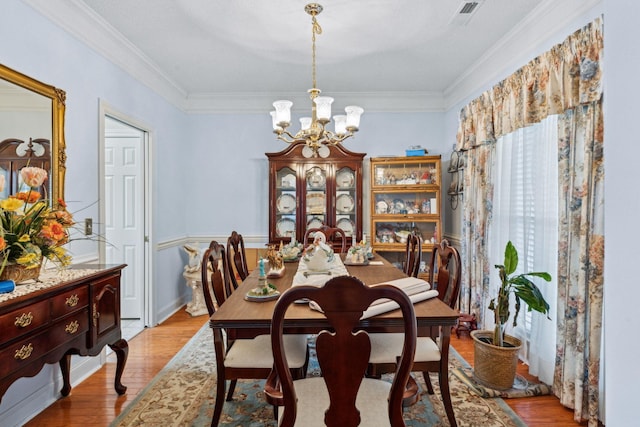 dining space featuring crown molding, a notable chandelier, and light hardwood / wood-style flooring