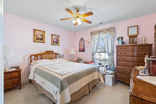 bedroom with ceiling fan, light colored carpet, and a textured ceiling