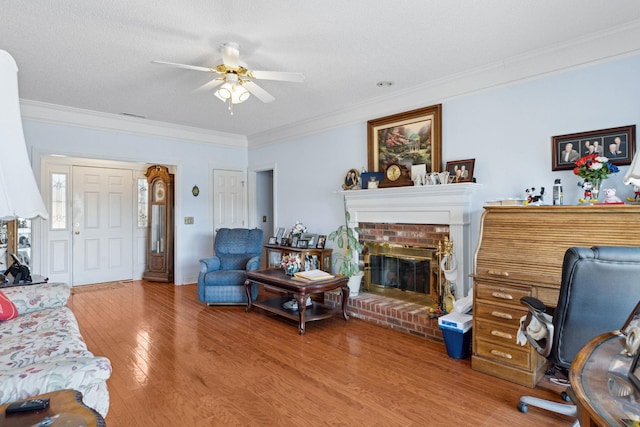 living room with crown molding, wood-type flooring, a textured ceiling, ceiling fan, and a fireplace