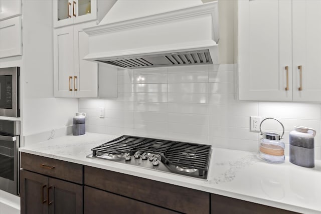  - kitchen with dark brown cabinets, glass insert cabinets, tasteful backsplash, custom range hood, and stainless steel appliances