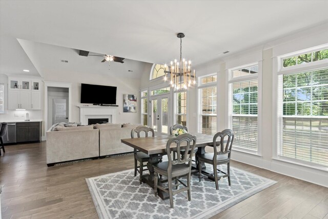  - dining area with french doors, a fireplace, vaulted ceiling, wood finished floors, and ceiling fan with notable chandelier