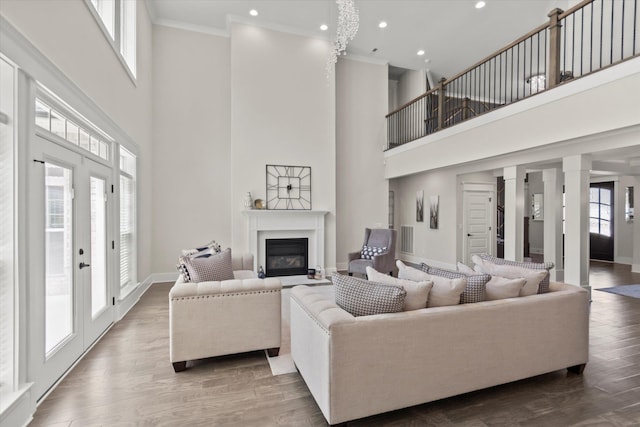  - living area featuring a glass covered fireplace, crown molding, visible vents, and a towering ceiling