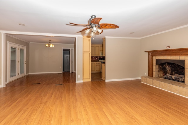 unfurnished living room with ceiling fan with notable chandelier, light hardwood / wood-style flooring, ornamental molding, and a tiled fireplace