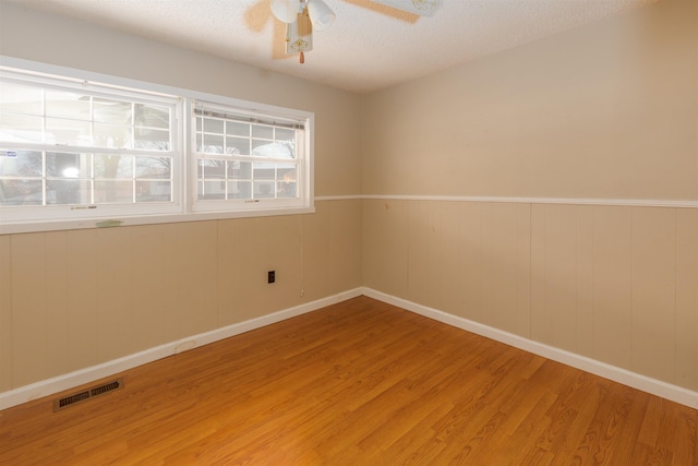 unfurnished room featuring hardwood / wood-style floors, ceiling fan, a textured ceiling, and wooden walls