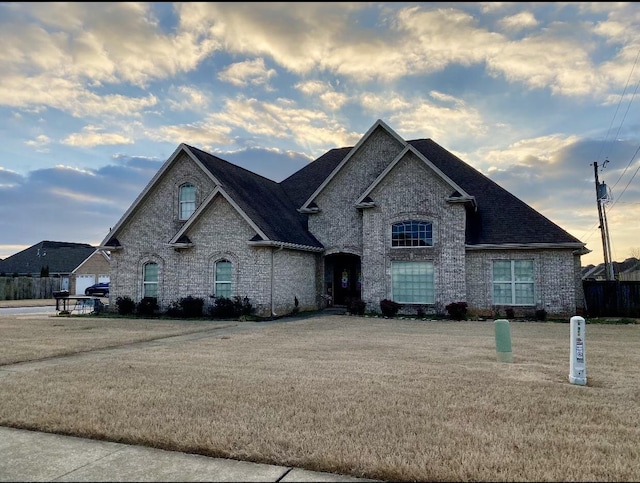 view of front of house featuring roof with shingles, a front lawn, and brick siding