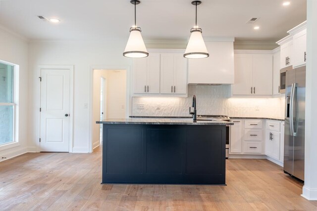 kitchen featuring white cabinetry, stainless steel refrigerator with ice dispenser, light hardwood / wood-style floors, decorative light fixtures, and a center island with sink