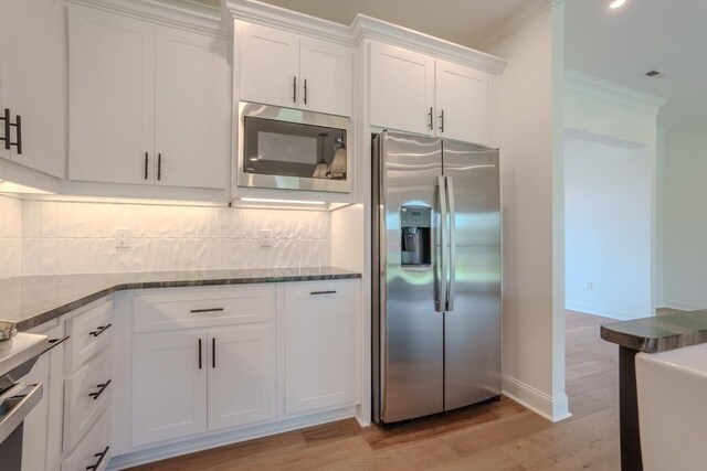 kitchen with white cabinets, crown molding, decorative backsplash, light wood-type flooring, and stainless steel appliances