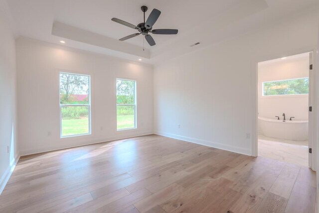 empty room with a raised ceiling, ceiling fan, and light hardwood / wood-style floors