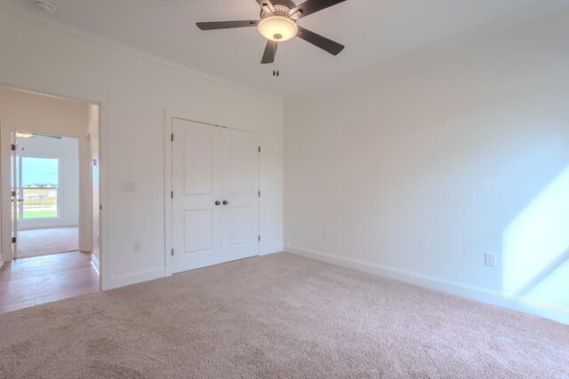 unfurnished bedroom featuring ceiling fan, ornamental molding, light carpet, and a closet