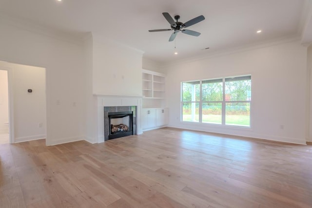 unfurnished living room with ceiling fan, crown molding, built in features, a fireplace, and light hardwood / wood-style floors