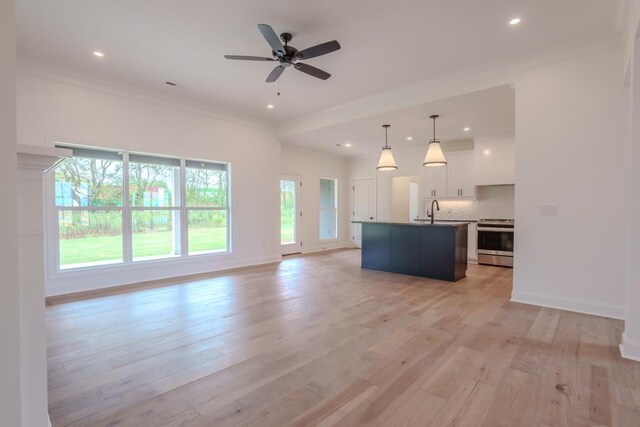 kitchen featuring pendant lighting, white cabinets, stainless steel stove, an island with sink, and tasteful backsplash