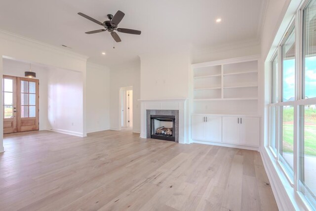 unfurnished living room with a tile fireplace, ceiling fan, french doors, crown molding, and light wood-type flooring