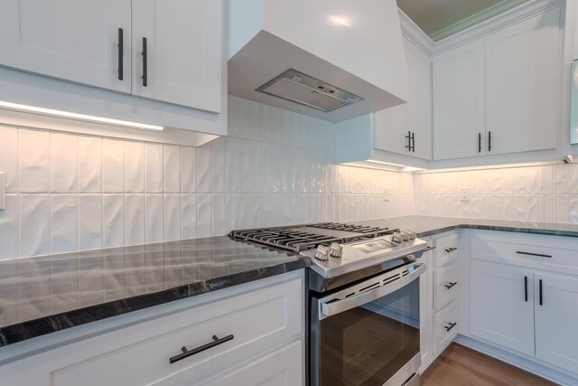 kitchen featuring gas range, white cabinetry, wall chimney exhaust hood, backsplash, and dark stone countertops