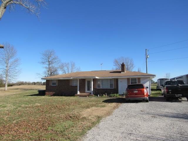 single story home with a front yard, gravel driveway, cooling unit, and a chimney