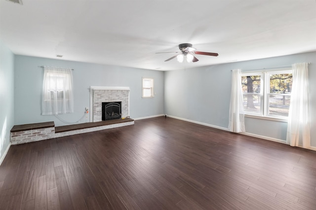 unfurnished living room featuring plenty of natural light, dark hardwood / wood-style floors, a fireplace, and ceiling fan