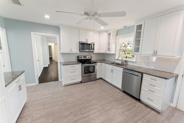 kitchen featuring appliances with stainless steel finishes, dark stone counters, ceiling fan, sink, and white cabinets