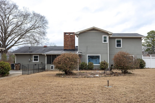 rear view of house with a sunroom, fence, a chimney, and a lawn