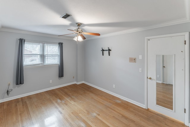 empty room featuring baseboards, light wood-style flooring, visible vents, and crown molding