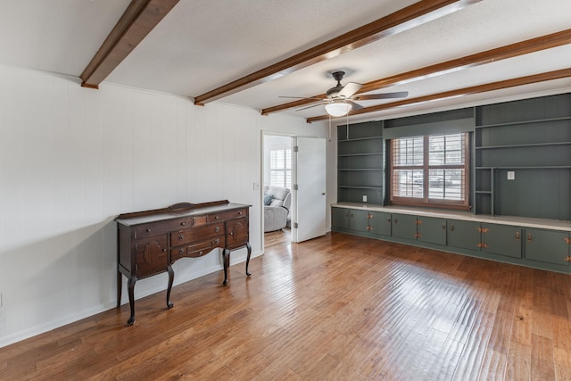 interior space with a textured ceiling, ceiling fan, built in shelves, light wood finished floors, and beamed ceiling