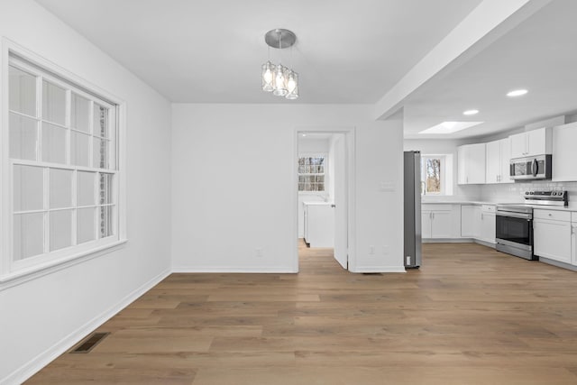 kitchen with decorative light fixtures, white cabinetry, backsplash, stainless steel appliances, and light wood-type flooring