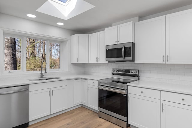 kitchen featuring white cabinetry, stainless steel appliances, sink, and light hardwood / wood-style flooring