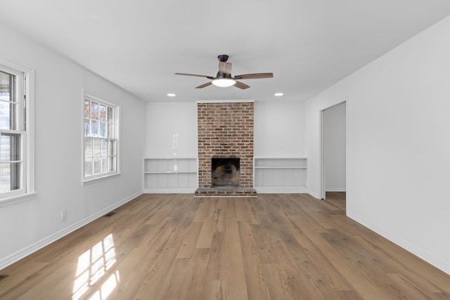 unfurnished living room with ceiling fan, a brick fireplace, and light wood-type flooring