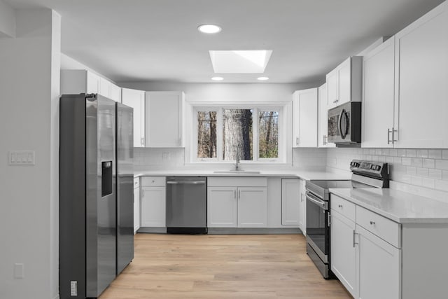 kitchen with sink, a skylight, white cabinets, stainless steel appliances, and backsplash