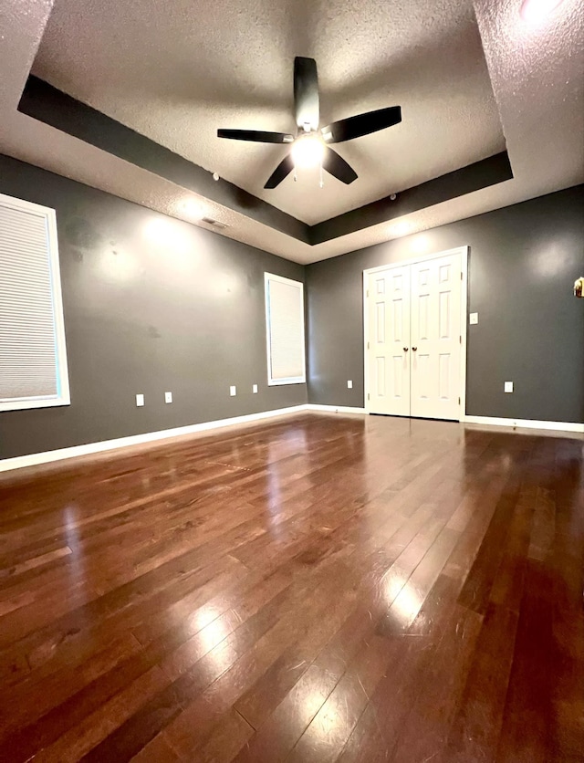 unfurnished bedroom featuring ceiling fan, wood-type flooring, a raised ceiling, and a textured ceiling