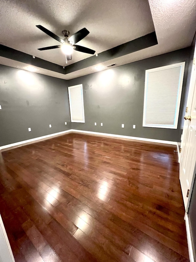 empty room with ceiling fan, dark hardwood / wood-style floors, a raised ceiling, and a textured ceiling