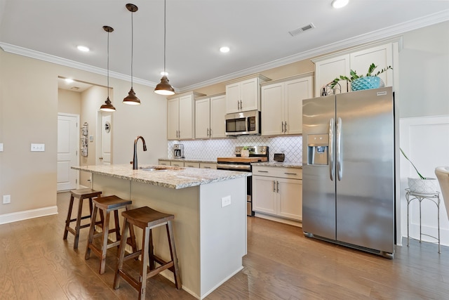 kitchen with crown molding, stainless steel appliances, visible vents, a kitchen island with sink, and a sink