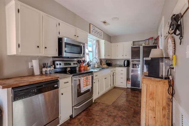 kitchen with wooden counters, stainless steel appliances, white cabinetry, and sink