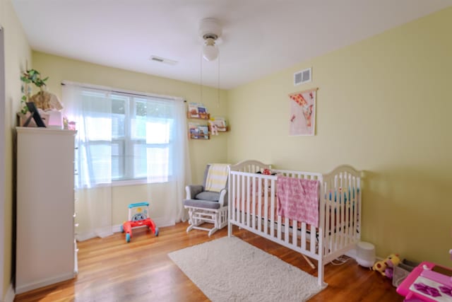 bedroom with ceiling fan, wood-type flooring, and a nursery area