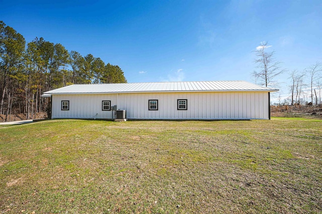 back of property featuring a pole building, central AC unit, metal roof, and a yard