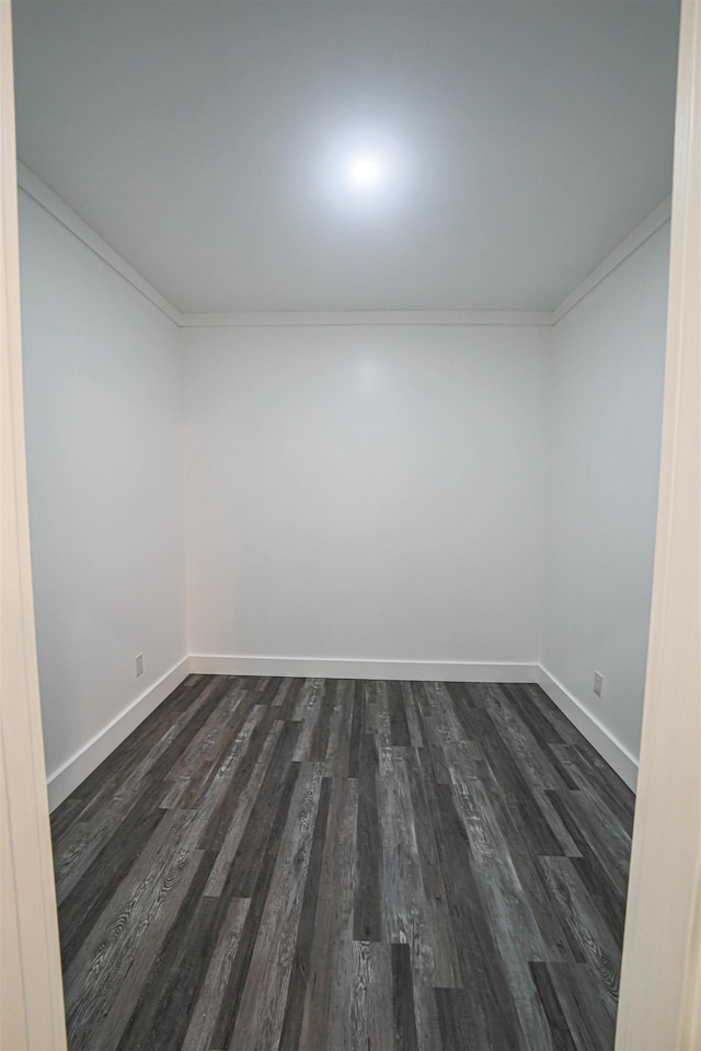 empty room featuring crown molding, dark wood finished floors, and baseboards