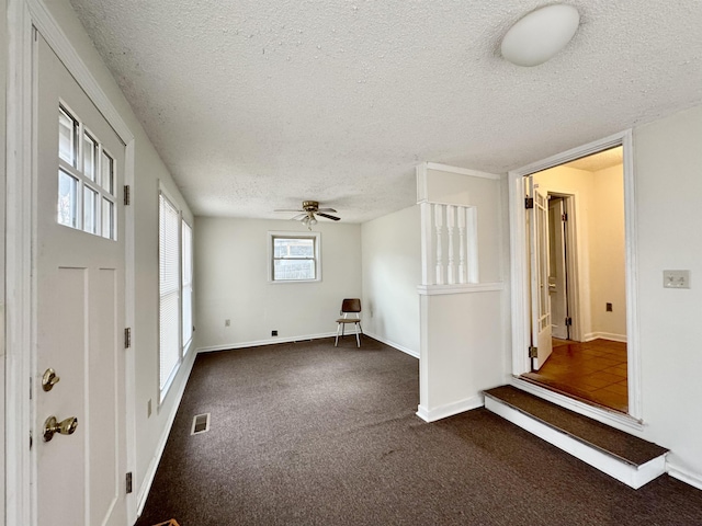 unfurnished room featuring ceiling fan, a textured ceiling, and dark colored carpet