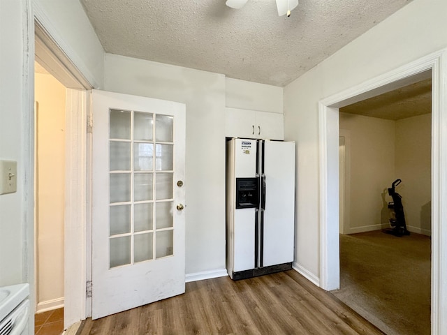 interior space with a textured ceiling, hardwood / wood-style flooring, ceiling fan, white refrigerator with ice dispenser, and white cabinets