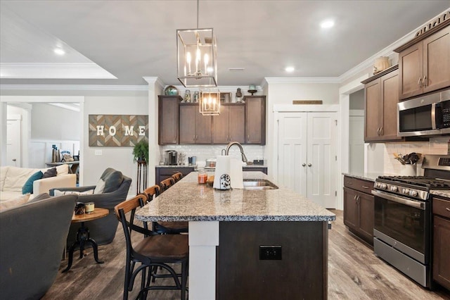 kitchen featuring light stone counters, sink, stainless steel appliances, and a center island with sink