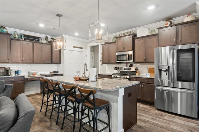 kitchen featuring light stone countertops, appliances with stainless steel finishes, a kitchen bar, a kitchen island with sink, and hanging light fixtures