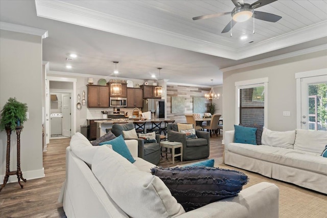 living room with dark hardwood / wood-style floors, washer / dryer, ornamental molding, and ceiling fan with notable chandelier