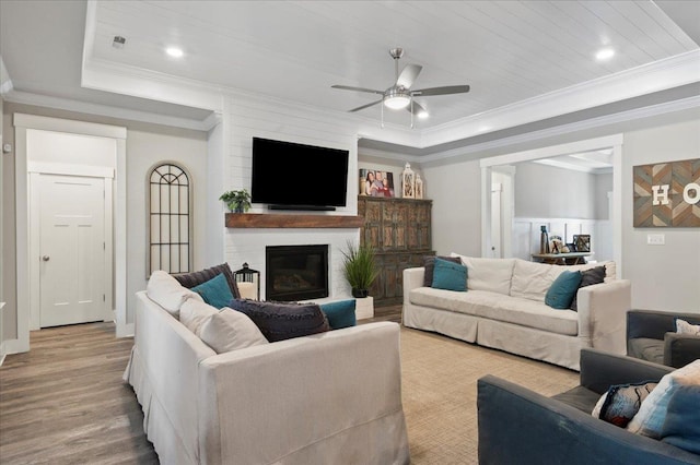 living room featuring ornamental molding, a tray ceiling, ceiling fan, light hardwood / wood-style flooring, and a fireplace