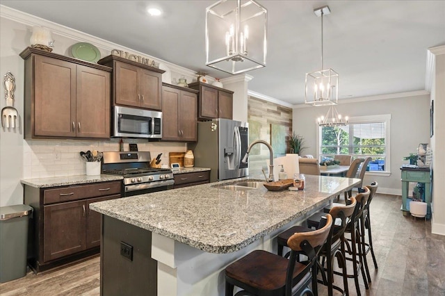 kitchen featuring a kitchen bar, sink, decorative light fixtures, light stone counters, and stainless steel appliances