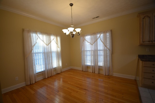 unfurnished dining area featuring crown molding, a chandelier, and light wood-type flooring