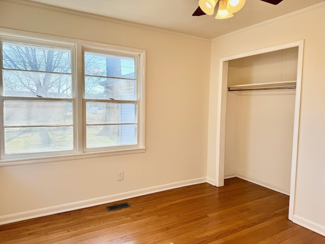 unfurnished bedroom with multiple windows, crown molding, wood-type flooring, and a closet