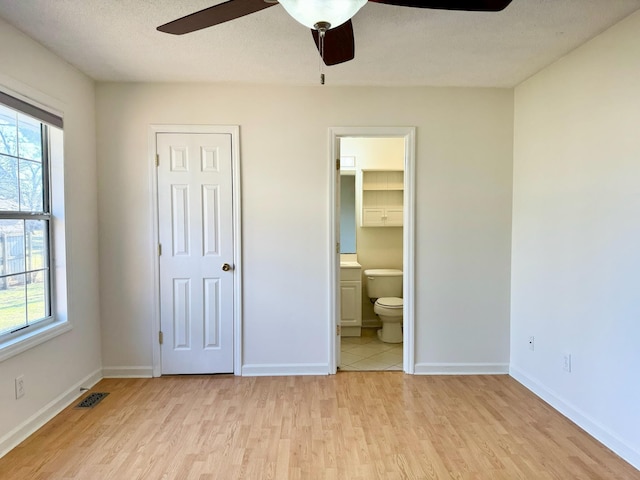 unfurnished bedroom featuring ceiling fan, ensuite bath, a textured ceiling, and light hardwood / wood-style flooring