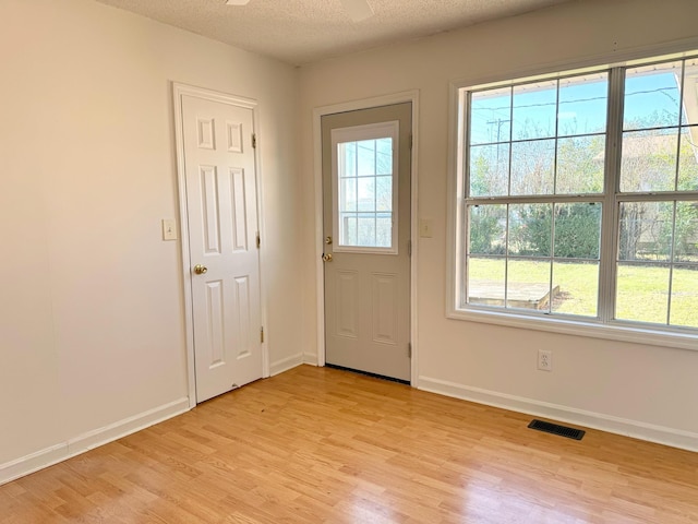 doorway to outside with plenty of natural light, light hardwood / wood-style floors, and a textured ceiling