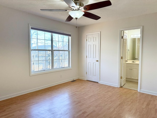 unfurnished bedroom featuring ceiling fan, ensuite bath, light hardwood / wood-style flooring, and a textured ceiling