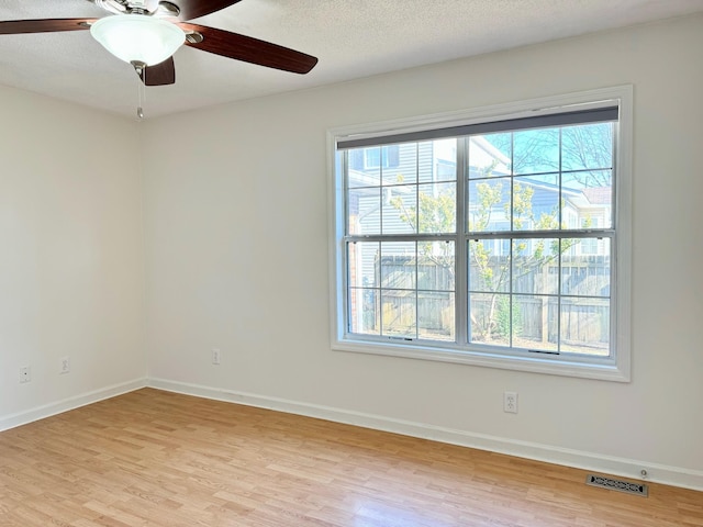 empty room with ceiling fan, a textured ceiling, a healthy amount of sunlight, and light wood-type flooring