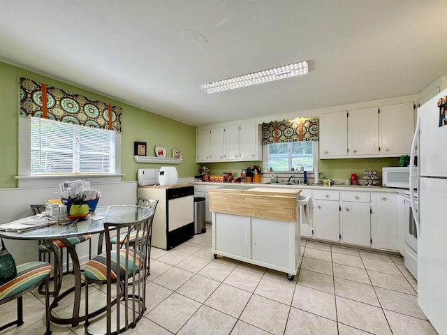  - kitchen with white appliances, white cabinets, light tile patterned floors, a wainscoted wall, and a center island