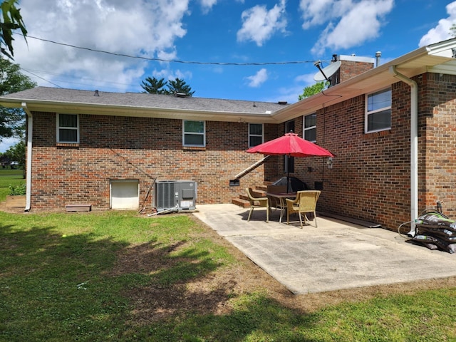 back of house featuring central air condition unit, a patio area, a lawn, and brick siding